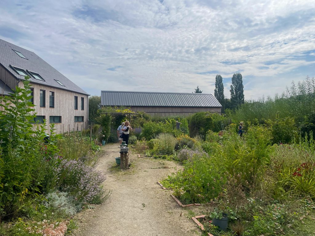 Des personnes marchent dans le jardin partagé du GAEC aux Prairies Saint-Martin, à Rennes, entouré de verdure.