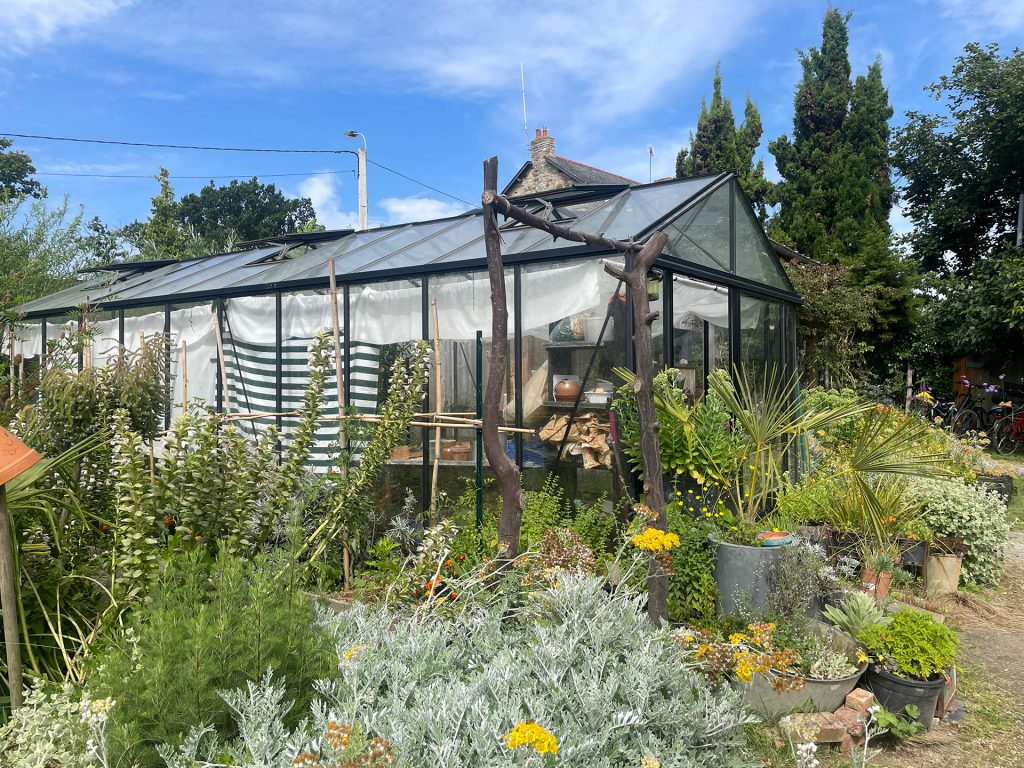 Vue de la serre du GAEC aux Prairie Saint-Martin, avec une grand variété de plantes devant le bâtiment