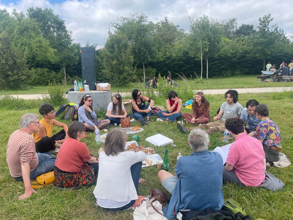 Un groupe de personnes assises en cercle sur l'herbe lors d'un pique-nique aux Prairies Saint-Martin en juin 2024