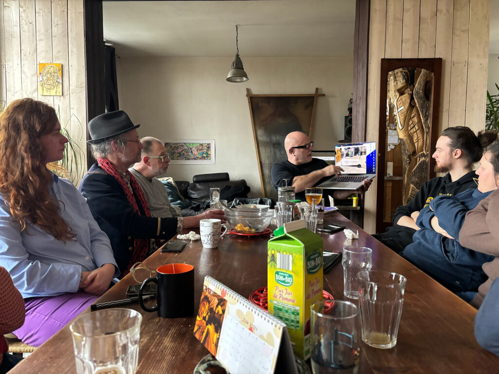 Le groupe de commanditaires assis à une table, Alex Herman, l’artiste, leur présente son travail sur son ordinateur.