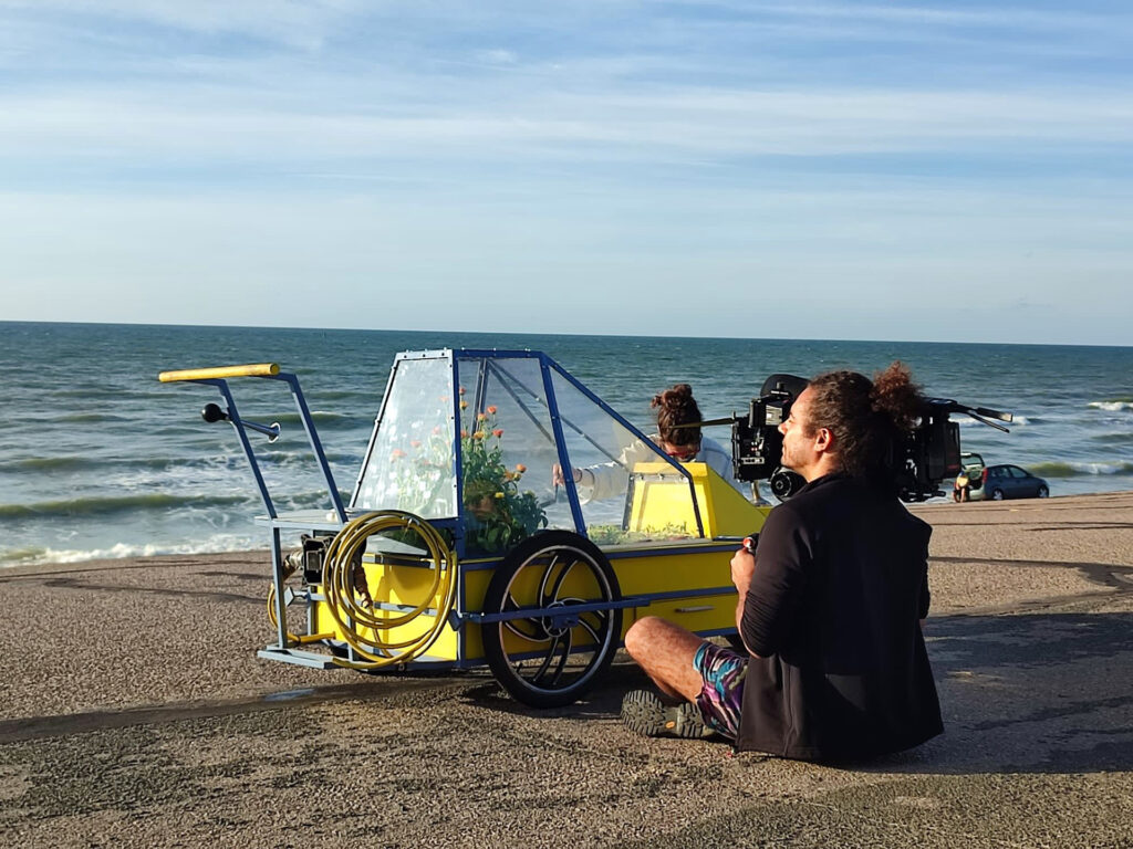 Un cameraman est assis sur la plage et film l’œuvre Cataplasme devant la mer