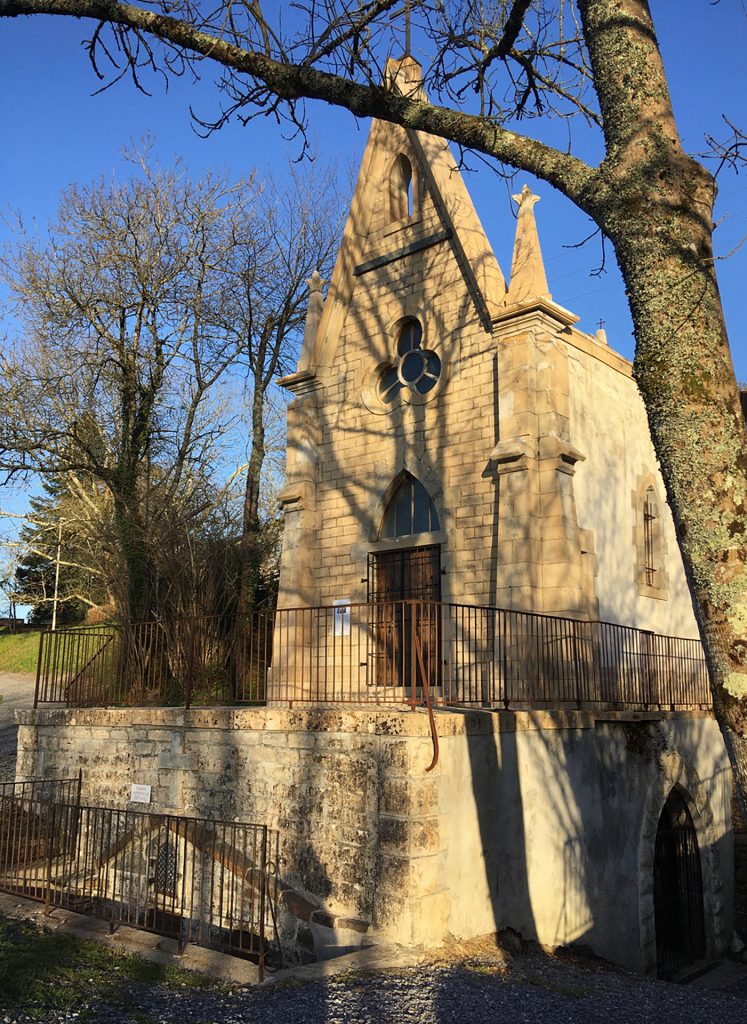 Vue de la chapelle néo-gothique depuis l’extérieur, un arbre sans feuille au premier plan et deux autres à côté de la chapelle illustrent la saison hivernale.