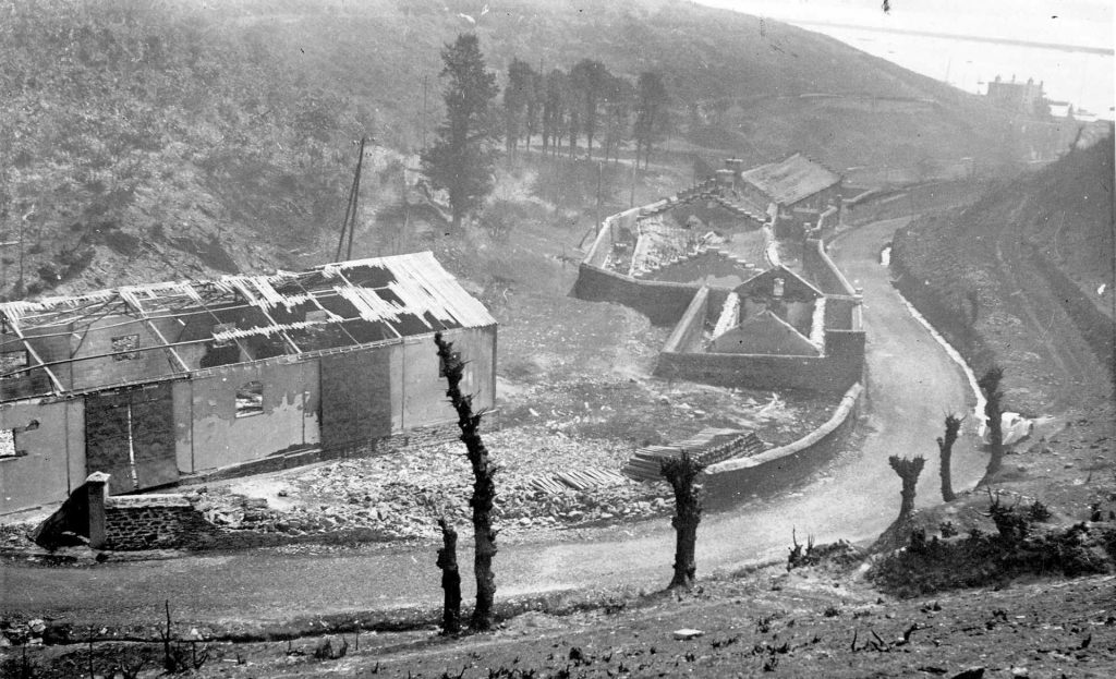 Image d’archive en noir et blanc d'une route avec des maisons, représentant les hauteurs de Maison Blanche après l'incendie des cuves de mazout en 1940.