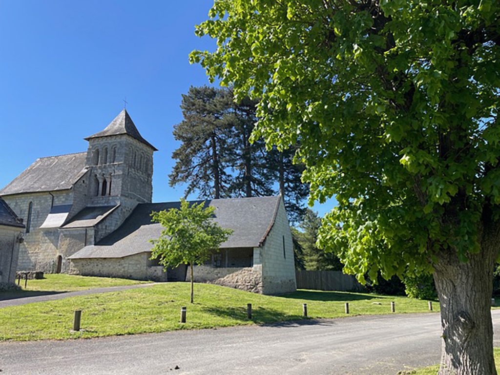 Vue de l'église du Prieuré, une route passe devant et un arbre est en premier plan.