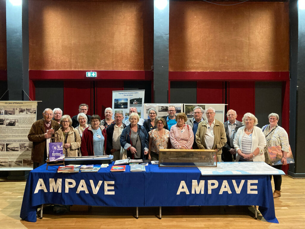 Un groupe de personnes, les commanditaires, posent devant une table avec la bannière « AMPAVE »