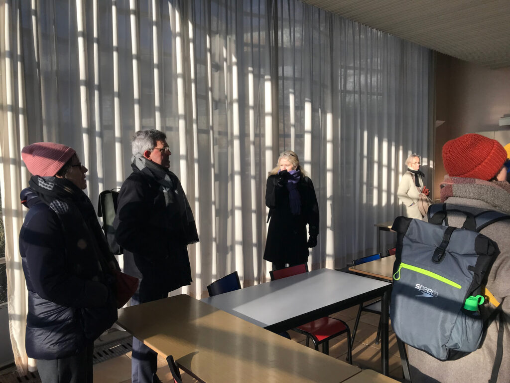 Dans une salle du futur site, plusieurs personnes sont debout près de table, habillées en manteau, lors de la visite.