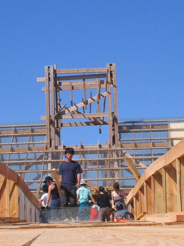 Un groupe de personne est visible sur la passerelle en construction. Le belvédère, lui aussi en construction, est visible en arrière-plan.