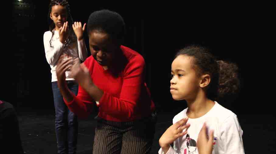 Une femme se tient entre deux jeunes filles. Elles dansent tout en signant avec leurs mains.