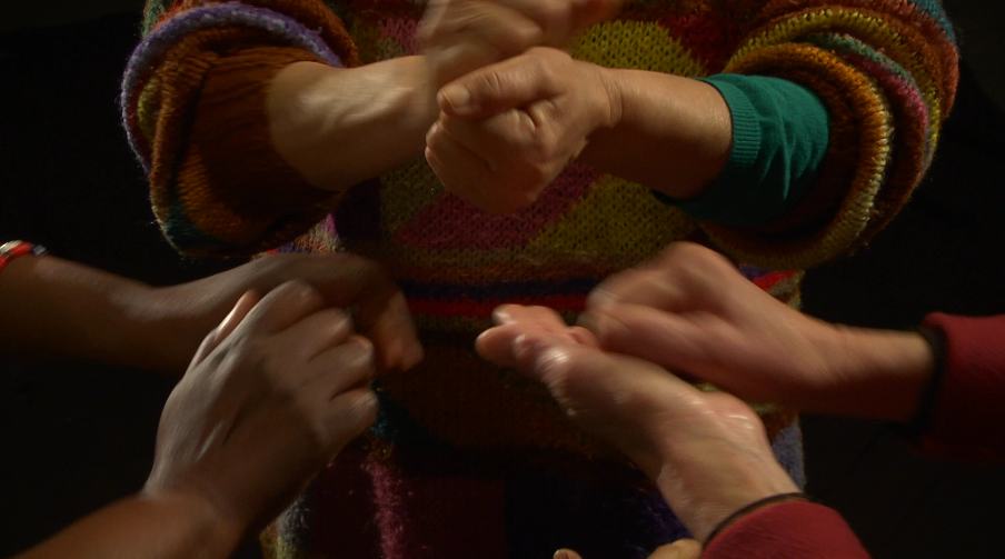Trois personnes en cercle positionnent leurs mains face à elles. Leurs mains sont en mouvement.