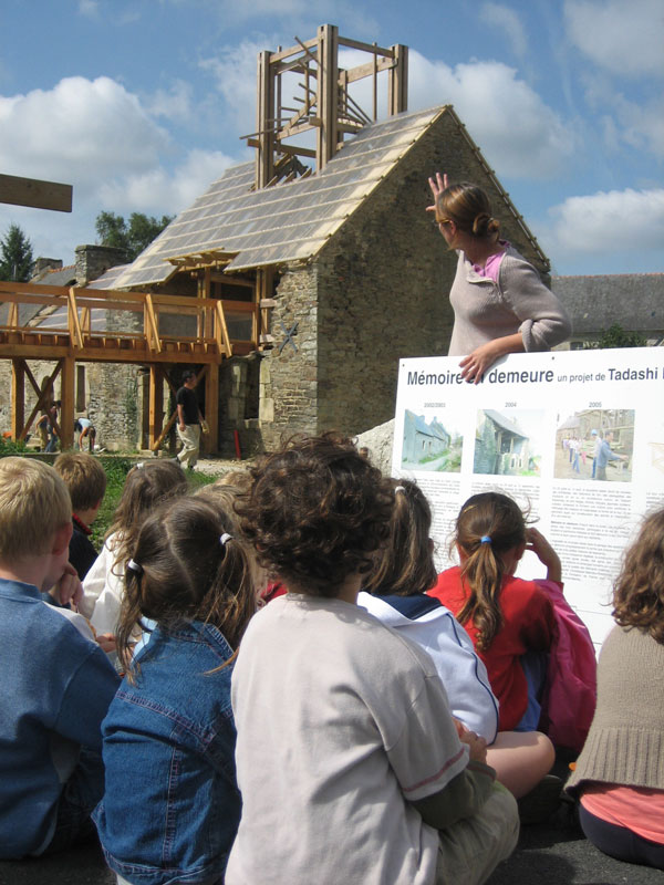 Un groupe d'enfant, assis devant le bâtiment du belvédère et de la passerelle, est en visite sur le site de réhabilitation.