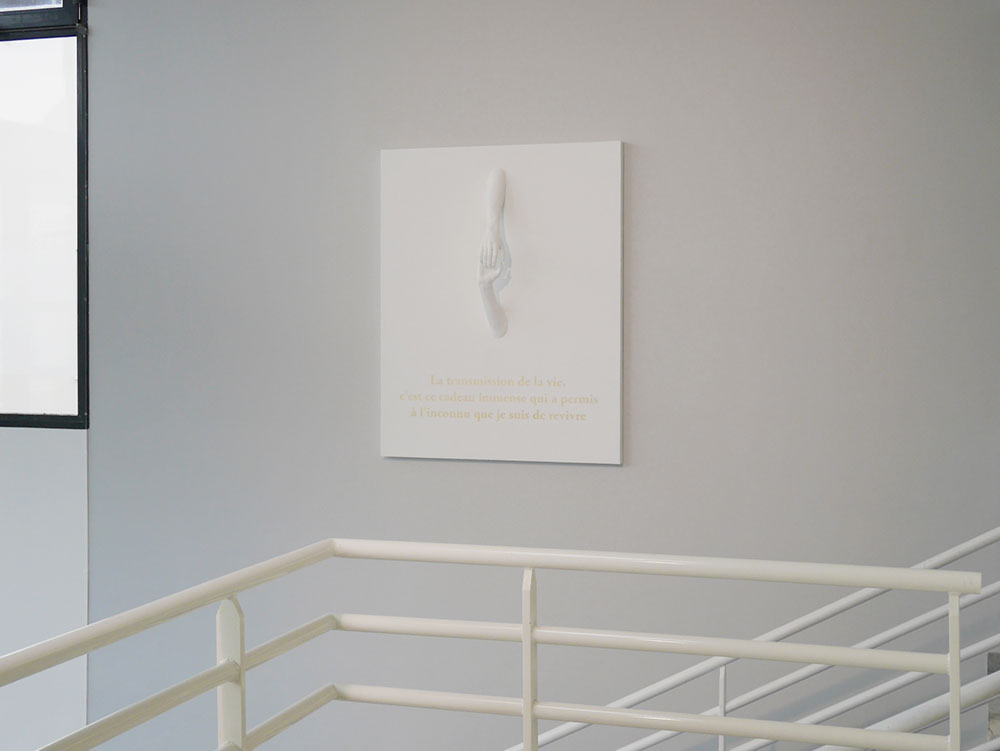 Sur le mur de l'escalier principal dans le hall d'entrée de l'hôpital Saint-Malo, un bas-relief représentant deux mains se tenant orne l'espace avec délicatesse.