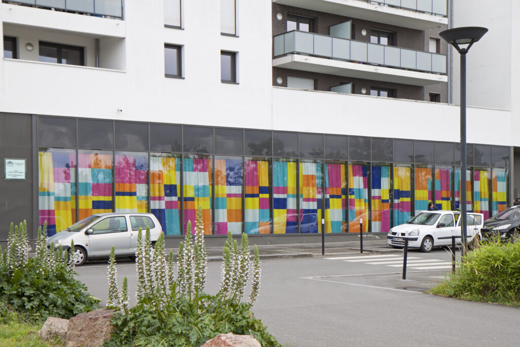 Depuis l'extérieur, le rideau attire l’œil des passants tout en ne permettant pas de voir l'intérieur. Les couleurs vives se détachent des tons sombres du bâtiment.